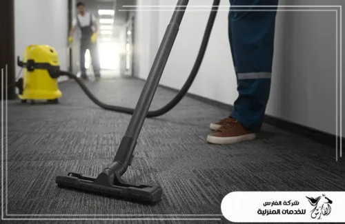 تنظيف موكيت بالدمام 0557756533 شركة الفارس عاملان ينظفان أرضية مغطاة بالسجاد الداكن بمكنسة كهربائية صناعية.