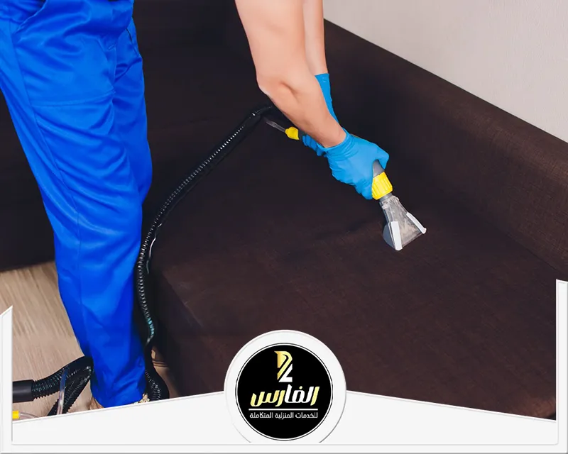 تنظيف مجالس بالرياض باستخدام جهاز تنظيف مخصص لإزالة الأوساخ من القماش مع استخدام قفازات لحماية اليدين.