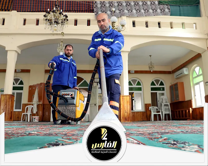 اثنان من الرجال في جاكيتات زرقاء ينظفان سجادة في مكان عبادة.