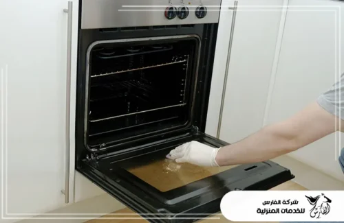 شركة تنظيف وصيانة افران غاز بالرياض 0557756533 الفارس عامل بقفاز أبيض يمسح الدهون المتراكمة على الباب الداخلي للفرن.