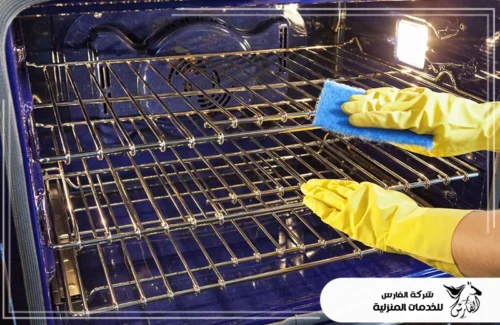 منظف افران سيراميك بالرياض 0557756533 الفارس أيدٍ ترتدي قفازات صفراء تنظف شبكة رفوف الفرن بفرشاة أو إسفنجة.