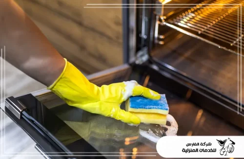 تنظيف فرن جليم غاز في الرياض 0557756533 شركة الفارس يد بقفاز أصفر تنظف الباب الزجاجي للفرن باستخدام إسفنجة صفراء وزرقاء.