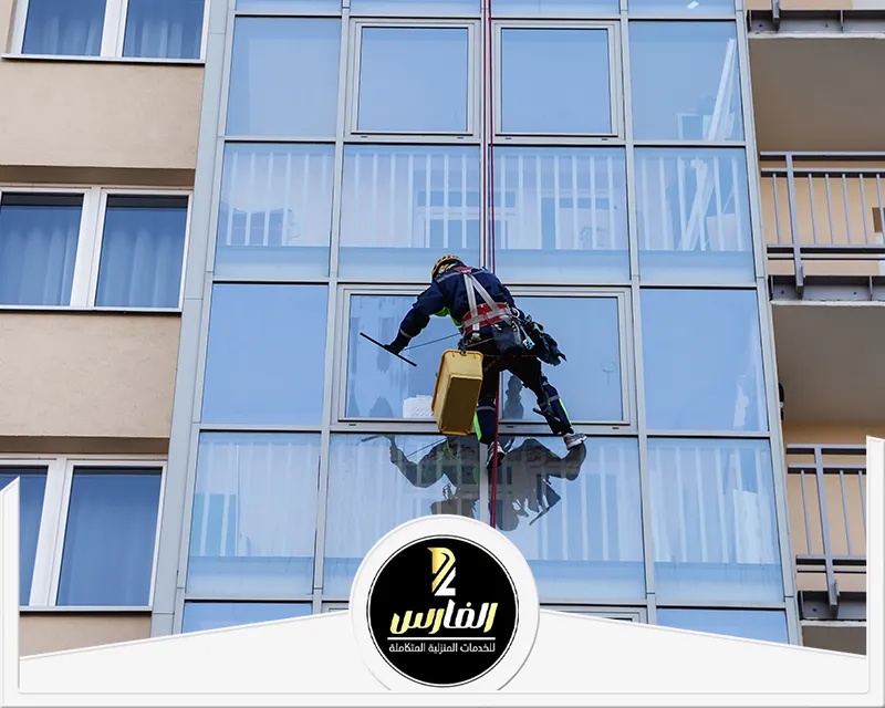 شركة تنظيف واجهات زجاج بالرياض 0557756533 شركة الفارس تنظيف واجهات زجاج بالرياض على ارتفاع باستخدام الحبال، مع عمال يرتدون معدات الحماية.
