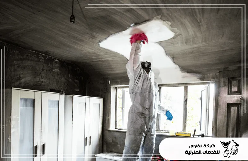شركة تنظيف البيت بعد الحريق بالرياض 0557756533 الفارس عامل يرتدي زي وقائي يقوم بتنظيف السقف المتضرر من الحريق، في إطار خدمات شركة الفارس للخدمات المنزلية.