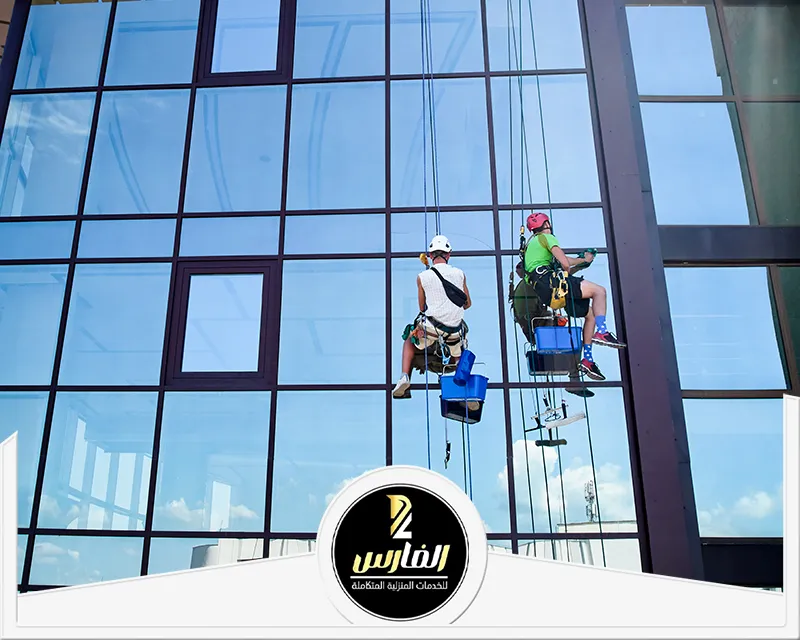 شركة تنظيف واجهات زجاج بالرياض 0557756533 شركة الفارس عمال يستخدمون الرافعة لتنظيف واجهة زجاجية بالرياض لمبنى تجاري عالٍ.